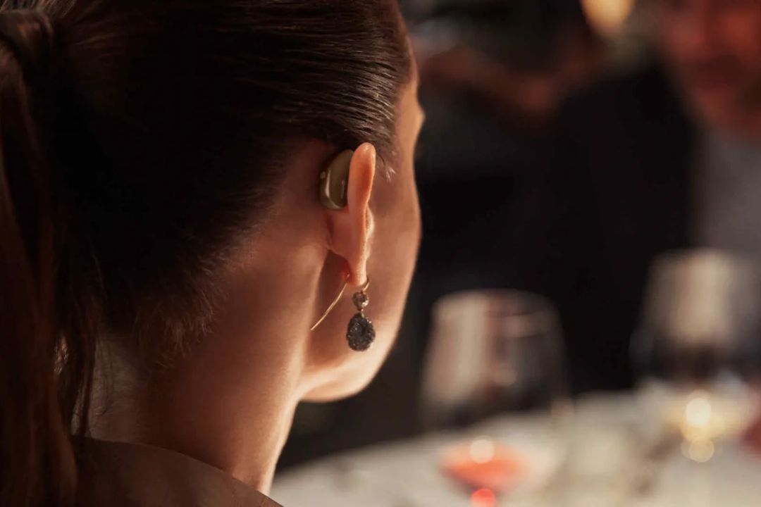 A close-up of a small hearing aid worn behind the ear at a dinner table