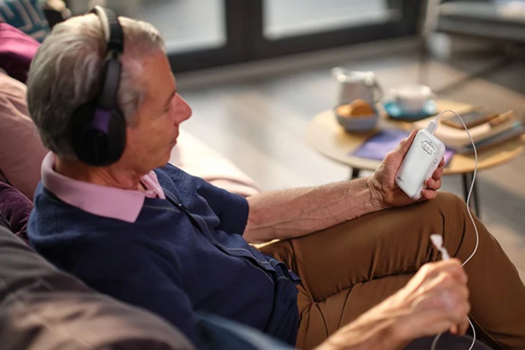 A man relaxing on a sofa using a Lenire handheld device with headphones