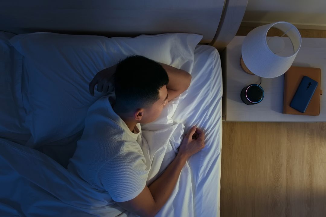 A person sleeping while a small speaker plays gentle sound on the nightstand