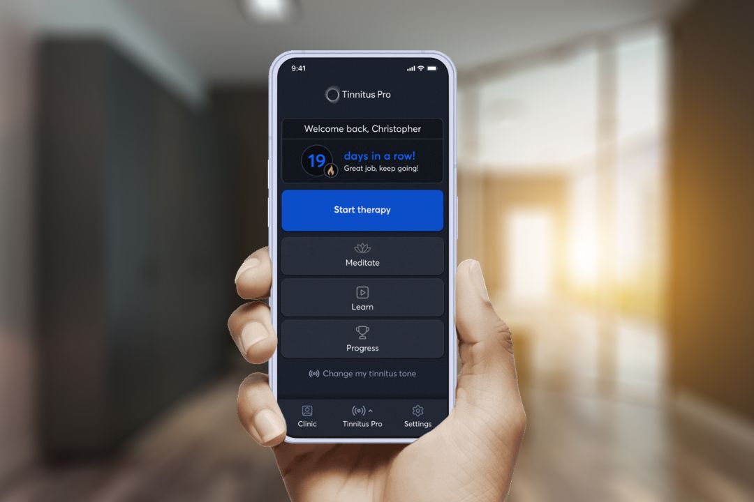 A hand holding a phone showing the Tinnitus Pro app's home screen